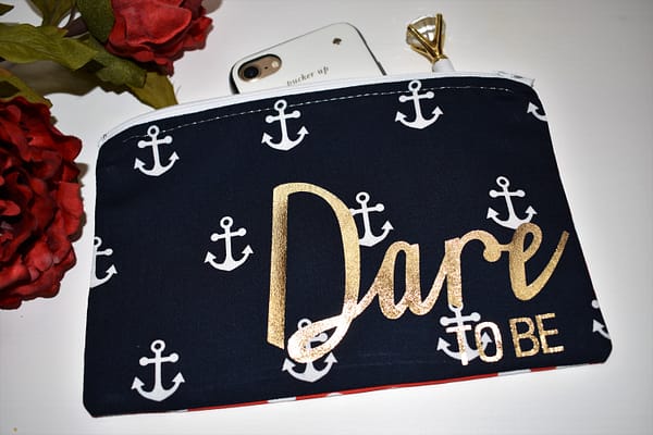 Zipper Pouch, Front: 'Dare to be' in gold, navy fabric with white anchors; white zipper