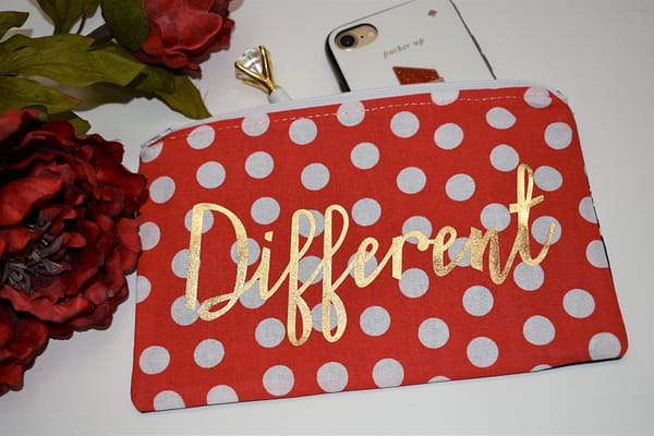 Zipper Pouch, Back: 'Different' in gold, red fabric with white polka dots; white zipper