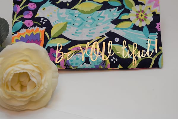 Zipper Pouch, Close-up: 'Be-YOU-tiful' in gold on navy fabric with mint green and white bird and colorful flowers of purple, fuchsia, orange, and yellow