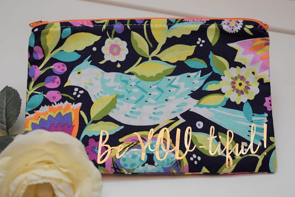 Zipper Pouch, Front: 'Be-YOU-tiful' in gold on navy fabric with mint green and white bird and colorful flowers of purple, fuchsia, orange and yellow; orange zipper